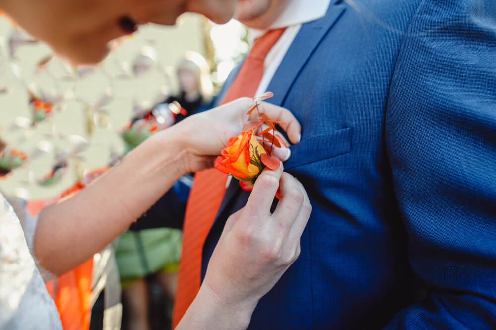 A bride pins the groom’s autumn boutonniere to his navy blue suit.;