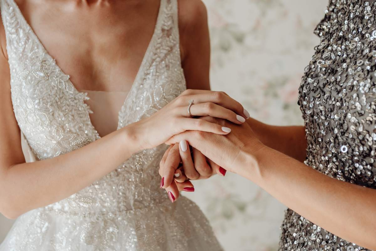 A heartfelt, close-up shot of the bride, and mother-of-the-bride, wearing a beautiful silver metallic dress.