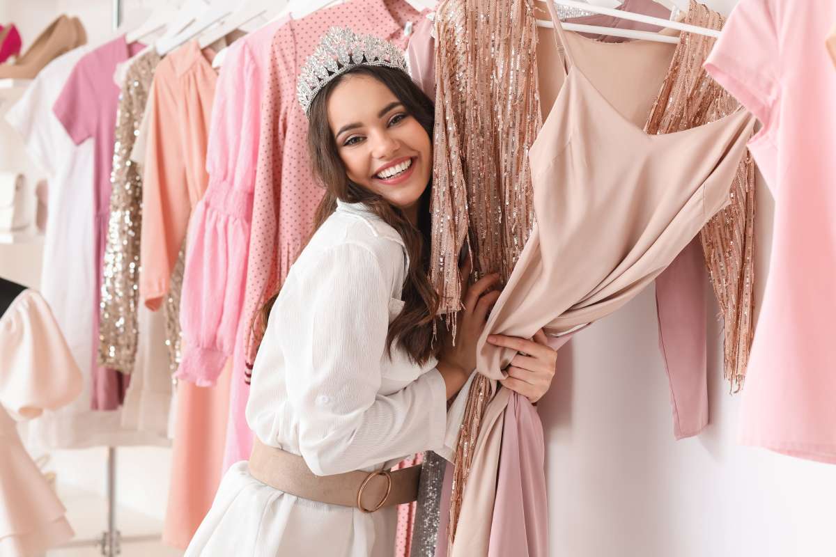 A young woman wearing a tiara, embracing various top trending prom dresses and smiling happily.