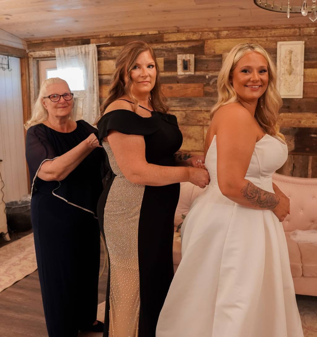 Bride in white with mother in slimming plus-size mother of the bride dresses in black and gold and grandmother in black.