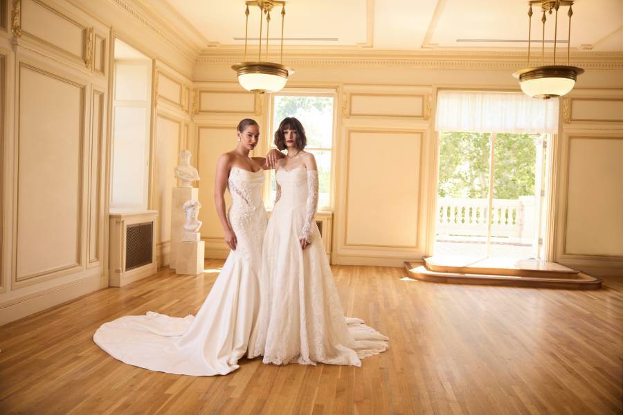 Two women standing together showing two wedding dresses