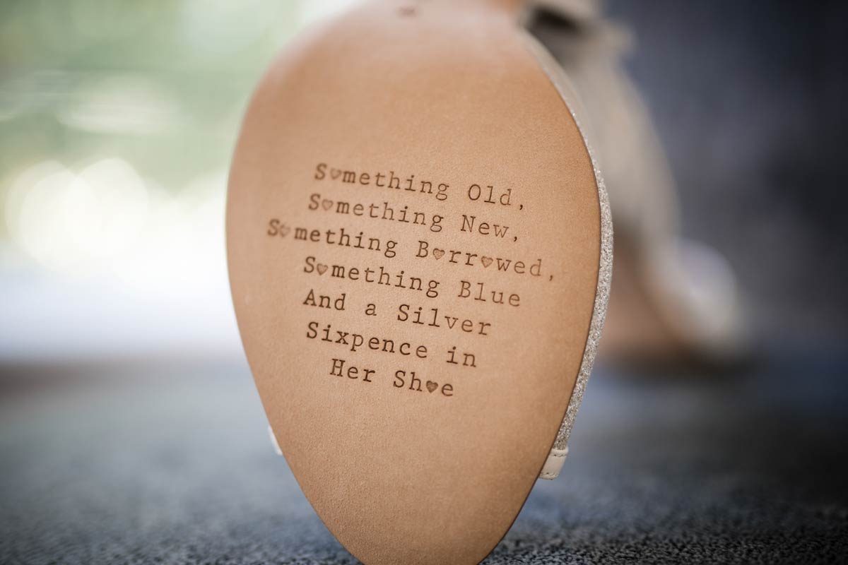 The bottom of a bride’s shoe with text that reads: something old, something new, something borrowed, something blue, and a silver sixpence in her shoe.