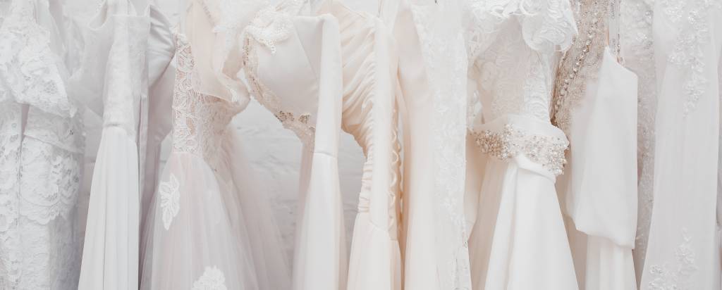 A rack showcases beautiful, white summer wedding dresses ready for hopeful brides to try on.